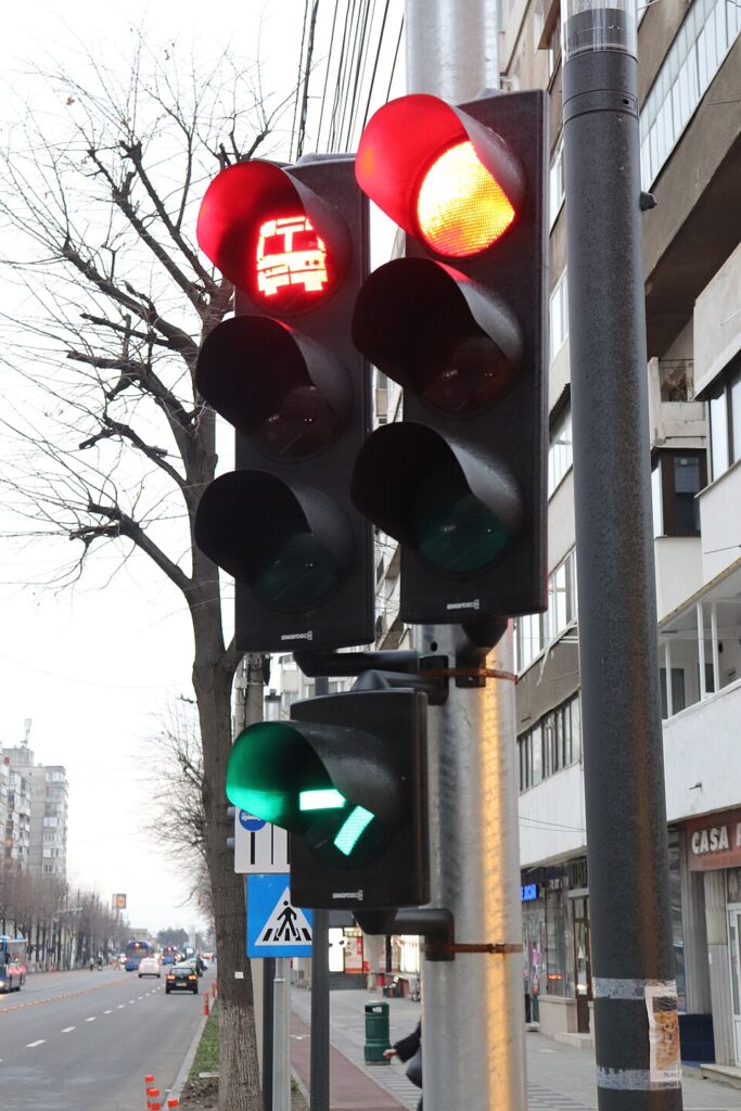 Semafor pe roșu, iar dedesubt lampa suplimentară cu săgeata verde aprinsă; în stânga, semaforul benzii de autobuz, cu autobuzul desenat în lumina roșie