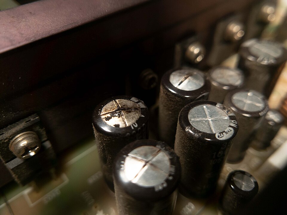 Condensatori electrolitici pe o placă, cu capacul bombat, iar unul cu supapa deschisă și urme de electrolit