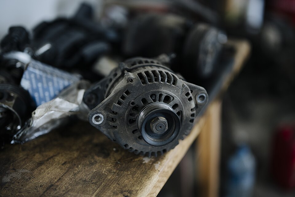 Alternator auto demontat, pe un banc de lucru din lemn, cu fulia și carcasa cu fante de aerisire în prim-plan